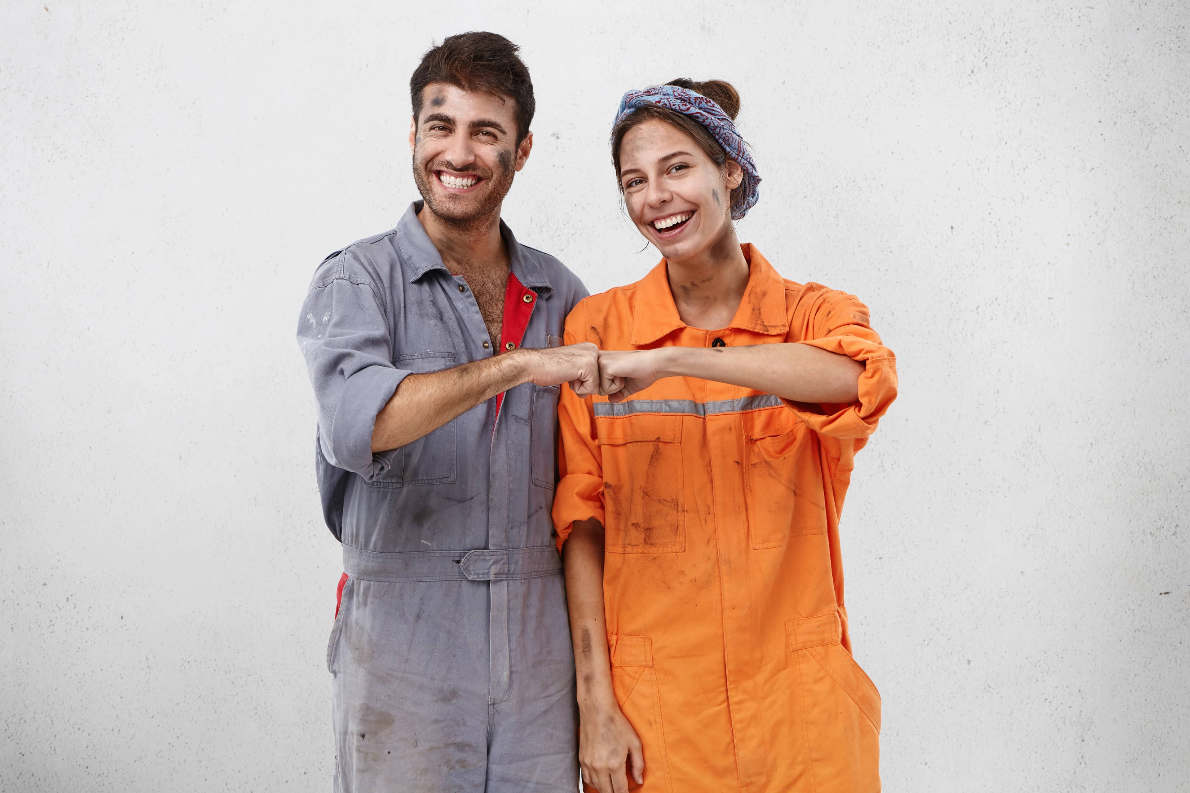 A man and a woman in Taskli working clothes fist bumping each other.